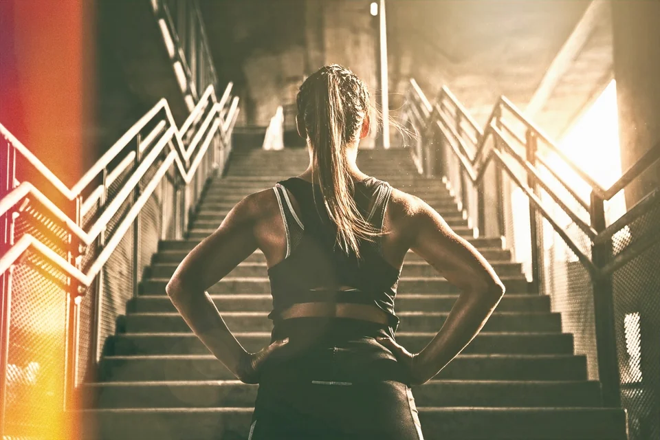 Une sportive face à un escalier, les mains sur les hanches, prête à avancer